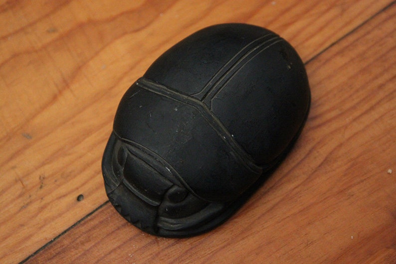 Puede incluir: Una escultura de escarabajo negro con detalles intrincados. La escultura est&aacute; hecha de un material liso y oscuro y tiene un acabado brillante.