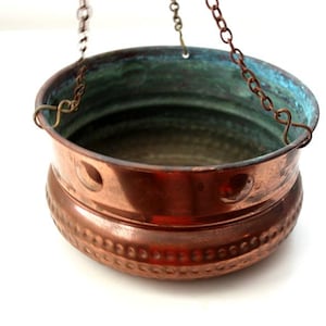 Peut inclure: Un pot de fleurs suspendu en cuivre avec une texture martelée et une chaîne pour l'accrocher. Le pot a une patine verte à l'intérieur.