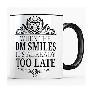 May include: White ceramic mug with a black rim and handle. The mug features a black and white graphic of a 20-sided die with a decorative border and the text "When the DM Smiles It's Already Too Late".