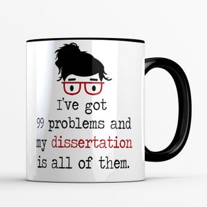May include: White coffee mug with a black rim and handle. The mug features a cartoon illustration of a person with glasses and the text "I've got 99 problems and my dissertation is all of them."