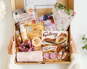 Puede incluir: Una caja de regalo de cartón marrón llena de varios artículos de cuidado personal, que incluyen una mascarilla facial, manteca de karité, una barra de chocolate y velas. La caja está abierta y los artículos son visibles. La caja tiene una etiqueta que dice "Just for you".