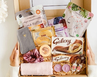 May include: A gift box containing a shea butter hand pack, a 24K gold eye mask, a Galaxy milk chocolate bar, a face mask, a gray fuzzy sock with a gold heart, a pink scrunchie, a pink washcloth, two purple tea light candles, and two candy rolls.
