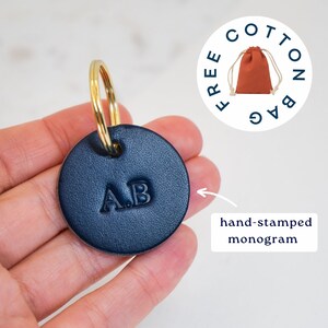 May include: A navy blue leather keychain with a gold key ring and the initials "A.B." hand-stamped on the front. It comes with a free cotton bag.