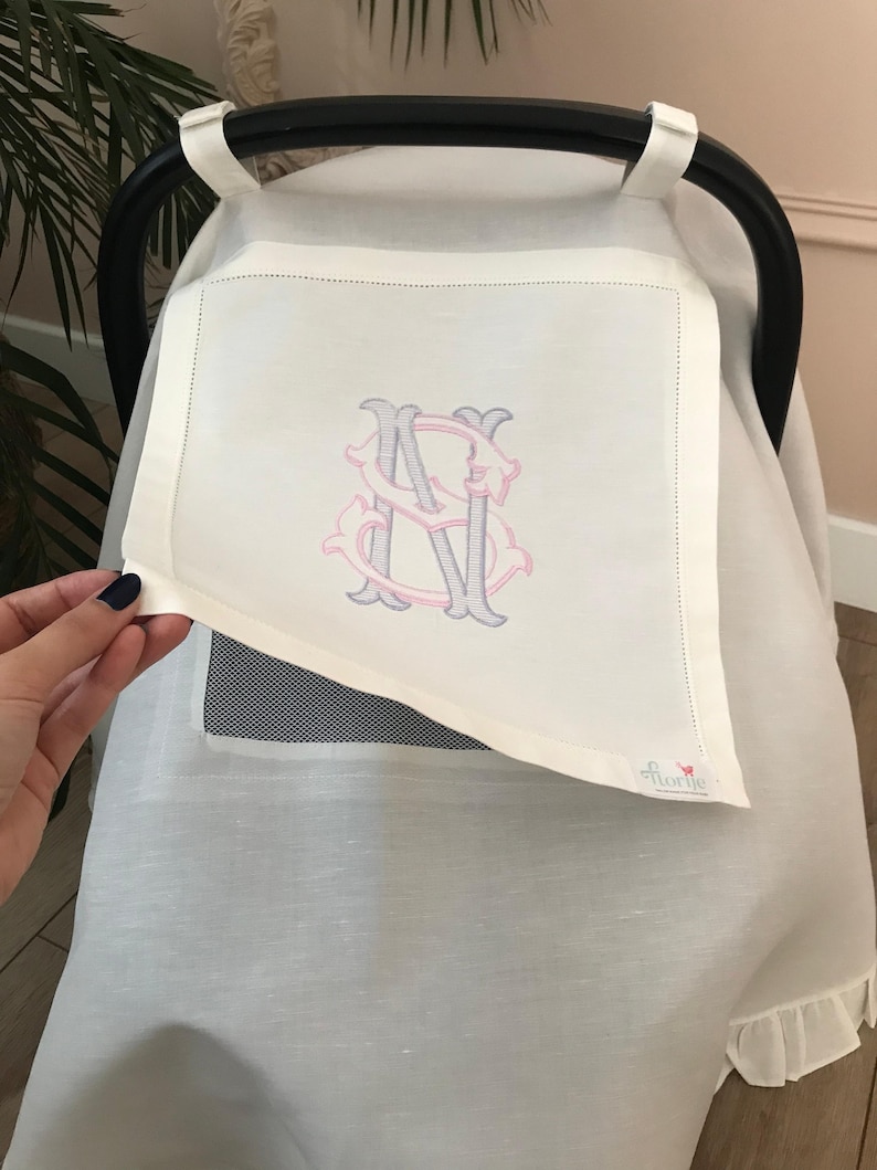 May include: White stroller cover with a monogrammed initial "S" in pink and gray embroidery. The cover has a mesh window and a ruffle trim. The brand name "florie" is embroidered in the bottom right corner.