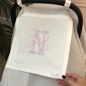 May include: White stroller cover with a pink and purple embroidered monogram "S". The cover has a small white tag with the word "florije" printed on it.