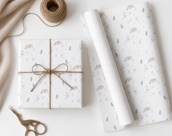 Könnte beinhalten: Ein rechteckiges Geschenk, eingewickelt in weißes Papier mit einem wiederkehrenden Muster aus kleinen braunen Igeln und grauem Blattwerk, gebunden mit braunem Bindfaden. Daneben liegt eine passende Rolle Geschenkpapier und eine goldene Schere.