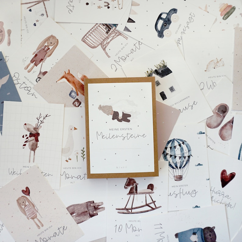 May include: A set of illustrated cards with a brown background and white text. The cards feature various illustrations of animals, objects, and activities. The text on the cards includes phrases like "My First Milestones", "Today I am 2 Months Old", and "My First Flight".