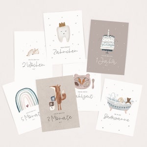 May include: Set of ten illustrated cards with milestones for a baby's first year. The cards feature a rainbow, a bunny, a tooth, a fox, a cake, and a bathtub. The cards are printed with the text "HEUTE BIN ICH" followed by the age in weeks, months, or years.