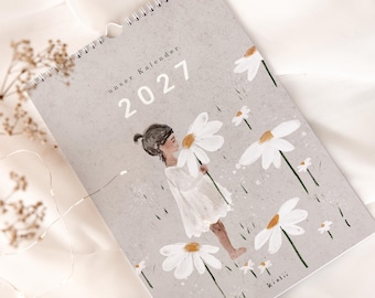 Peut inclure: Un calendrier mural à reliure spirale pour l'année 2027 avec une couverture gris clair mouchetée. La couverture présente une illustration d'une personne en robe blanche tenant une grande marguerite blanche, entourée d'autres marguerites.