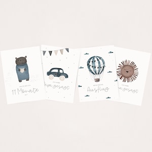 May include: Four illustrated cards with watercolor designs. The first card features a brown bear wearing a blue sweater and holding a blue heart. The text reads "Heute bin ich 11 Monate alt". The second card features a blue car with a white number one on the side. The text reads "Ich habe Papa gesagt". The third card features a blue and white hot air balloon with flags. The text reads "Mein erster Ausflug". The fourth card features a brown lion with closed eyes. The text reads "Ich habe Mama gesagt".