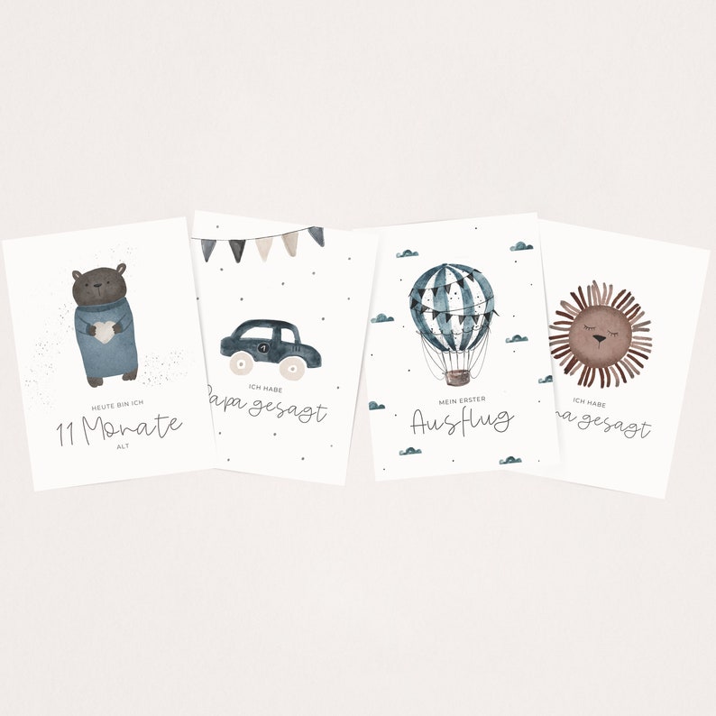 May include: Four illustrated cards with watercolor designs. The first card features a brown bear wearing a blue sweater and holding a blue heart. The text reads "Heute bin ich 11 Monate alt". The second card features a blue car with a white number one on the side. The text reads "Ich habe Papa gesagt". The third card features a blue and white hot air balloon with flags. The text reads "Mein erster Ausflug". The fourth card features a brown lion with closed eyes. The text reads "Ich habe Mama gesagt".
