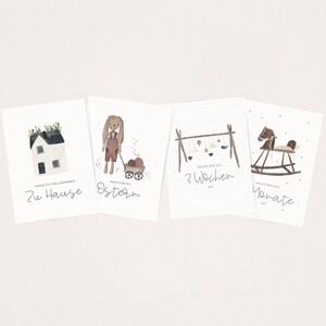 May include: Four illustrated cards with watercolor designs. The first card features a house with a green roof and the text "Herzlich Willkommen Zu Hause". The second card features a bunny holding a basket of eggs with the text "Mein Erstes Ostern". The third card features a mobile with the text "Heute bin ich 3 Wochen alt". The fourth card features a rocking horse with the text "Heute bin ich Monate alt."