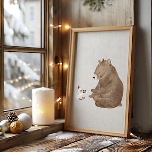 May include: A framed illustration of a brown bear sitting and looking at a small white animal with red accents. The background is a light brown with a subtle texture. The frame is a light brown wood.