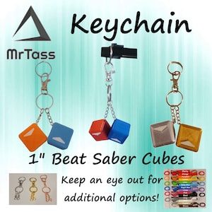 May include: A keychain featuring two 1-inch Beat Saber cubes, one red and one blue, with a white logo on each. The keychain is attached to a silver chain and a silver ring. The image also includes a variety of other keychain options in different colors.