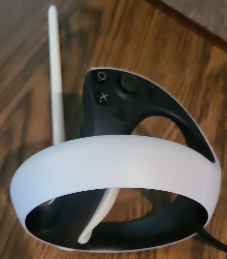 Puede incluir: Un auricular VR blanco y negro con una diadema blanca y un mando negro. El mando tiene un bot&oacute;n blanco y un bot&oacute;n X blanco.