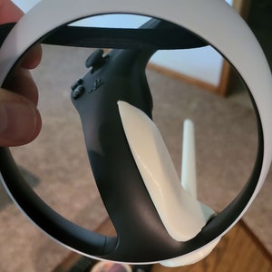 Puede incluir: Un auricular VR blanco con un mando negro conectado. El mando tiene una empu&ntilde;adura blanca y un bot&oacute;n negro.
