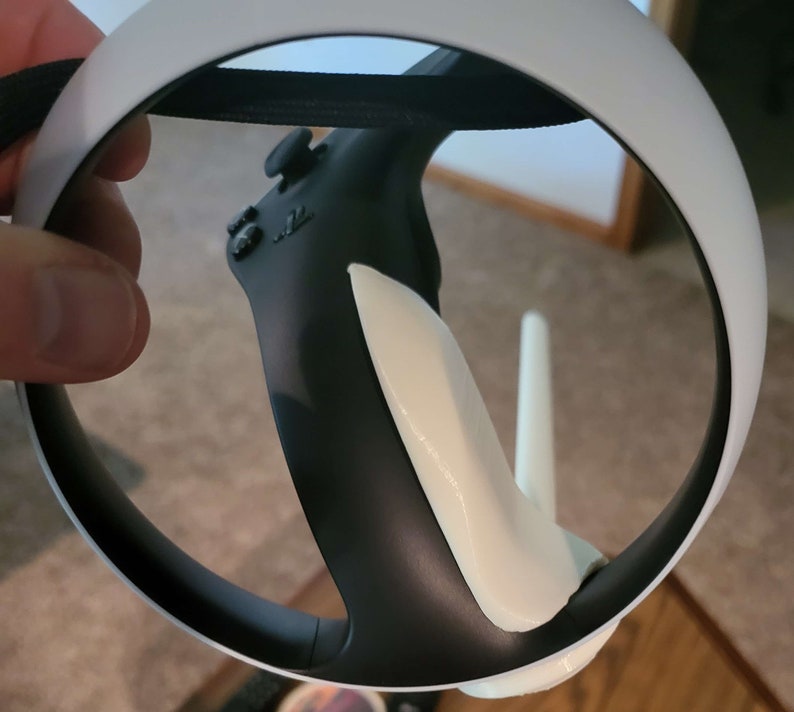 Puede incluir: Un auricular VR blanco con un mando negro conectado. El mando tiene una empu&ntilde;adura blanca y un bot&oacute;n negro.