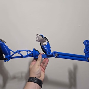 May include: A blue and black medical device, possibly a crutch or support, held against a white wall. The device has a curved design with a padded black section, a white support, and a series of blue, geometric components.