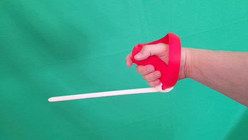 Puede incluir: Una f&eacute;rula de mano roja con una correa blanca. La f&eacute;rula est&aacute; dise&ntilde;ada para ayudar con la rehabilitaci&oacute;n de la mano.