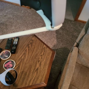 Puede incluir: Un auricular de realidad virtual blanco con una correa negra y una almohadilla de espuma blanca. El auricular est&aacute; apoyado en una mesa de madera con un mando a distancia y posavasos.