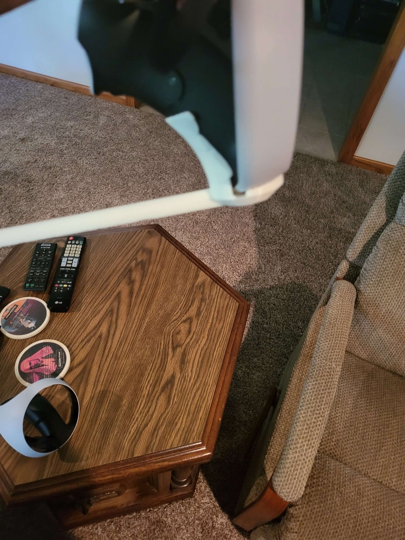 Puede incluir: Un auricular de realidad virtual blanco con una correa negra y una almohadilla de espuma blanca. El auricular est&aacute; apoyado en una mesa de madera con un mando a distancia y posavasos.