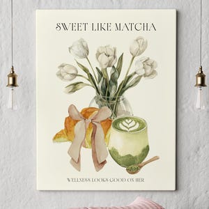 May include: A canvas print with a watercolour illustration of a matcha latte, tulips, and a croissant with a bow. The text reads "Sweet Like Matcha" and "Wellness Looks Good On Her". Two decorative pillows are below the print.
