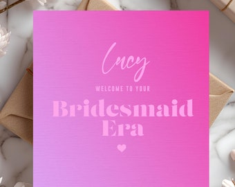 May include: Pink and white gradient card with the text "Welcome to your Bridesmaid Era" and the name "Lucy" written in cursive. The card has a small heart at the bottom and the text "SOLATAIRES" at the bottom.