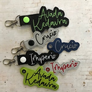 Puede incluir: Cinco llaveros diferentes con varios colores y diseños. Cada llavero presenta un hechizo diferente de Harry Potter escrito en cursiva: Avada Kedavra, Crucio, Imperio, Avada Kedavra y Crucio.