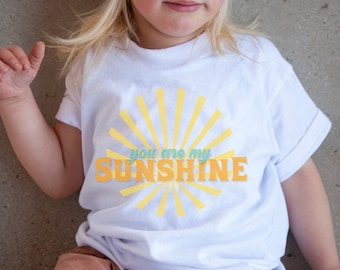 Może przedstawiać: Biała koszulka z żółtym nadrukiem słońca i tekstem "You are my sunshine".