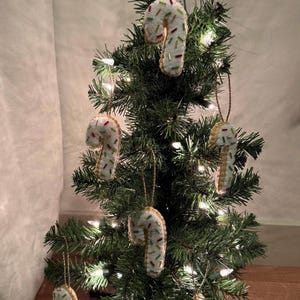 May include: A small Christmas tree decorated with handmade candy cane ornaments. The candy canes are white with colorful sprinkles and hang from the tree with gold string. The tree is lit with small white lights.