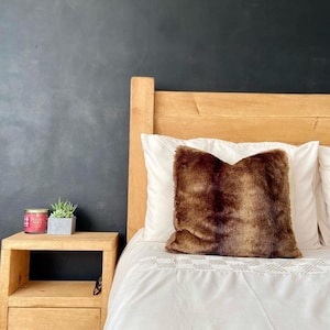 May include: A wooden bed frame with a white duvet and a brown faux fur pillow. A small wooden nightstand with a candle and two succulents sits next to the bed.