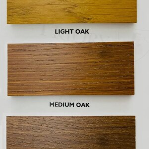 May include: Three rectangular wood samples showcasing different oak wood tones. The top sample is light oak, the middle is medium oak, and the bottom is dark oak. Each sample has the name of the wood tone printed below it.