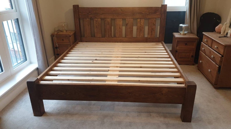Puede incluir: Un marco de cama de madera marr&oacute;n oscuro con una cabecera de listones y una base de listones. El marco de cama est&aacute; en un dormitorio con una mesita de noche y una c&oacute;moda.