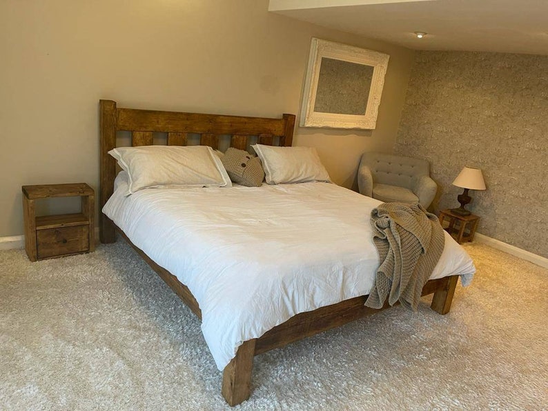 May include: A rustic wooden bed frame with a white duvet and pillows. The bed is in a bedroom with a white rug, a wooden nightstand, and a chair.