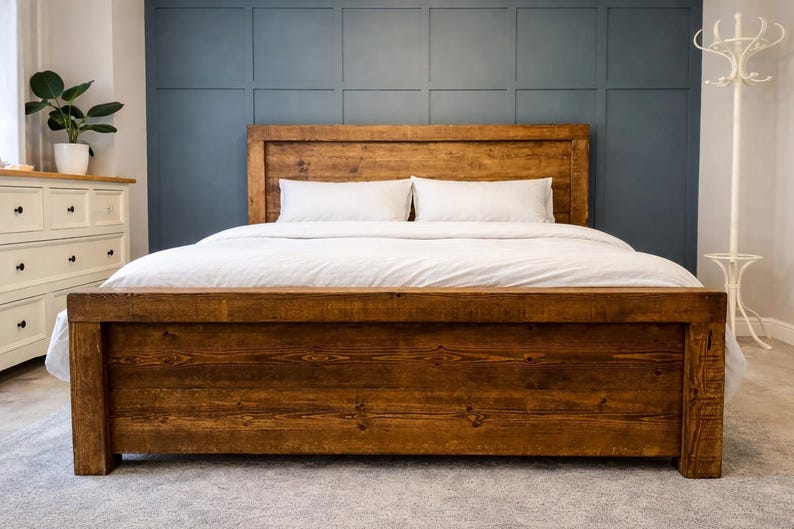 Puede incluir: Una cama de madera r&uacute;stica con cabecero y piecero. La cama est&aacute; hecha de madera te&ntilde;ida oscura y tiene un dise&ntilde;o rectangular simple. La cama est&aacute; cubierta con ropa de cama y almohadas blancas. El fondo es una pared azul oscuro.