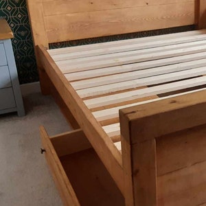 Puede incluir: Una estructura de cama de madera con cabecero y un caj&oacute;n abierto. La estructura de la cama es de madera de color claro y tiene una base de listones. El cabecero est&aacute; hecho de tablones de madera horizontales. El texto en la parte inferior dice "cajones bajo la cama no incluidos - consulte nuestros otros listados."