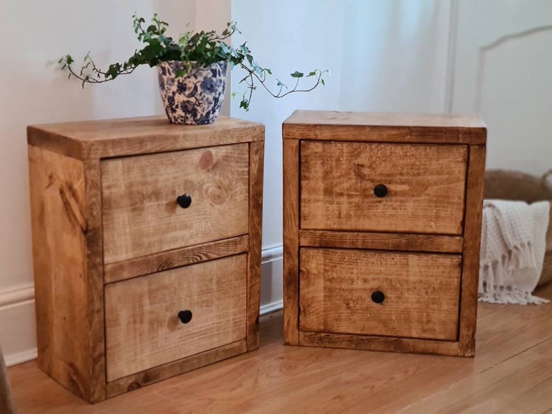 May include: Two wooden nightstands with two drawers each. The nightstands are made of reclaimed wood and have a rustic finish. The drawers have black metal knobs.