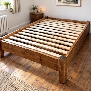May include: A low-profile bed frame constructed from dark stained wood with a visible grain pattern. The frame features four sturdy corner posts and a series of light-coloured, unfinished wooden slats arranged horizontally to support a mattress.