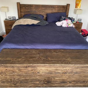 K&ouml;nnte beinhalten: Ein dunkelbraunes Holzbettgestell mit einer blauen Bettdecke und einem passenden Holz-Fu&szlig;teil mit Stauraum. Das Bett ist aus dunkelbraunem Holz gefertigt und hat ein schlichtes Design.