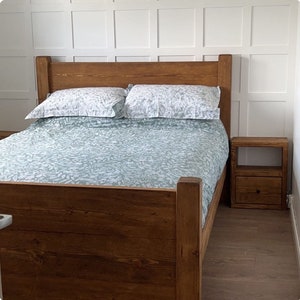 May include: A wooden bed frame with a headboard, a bedspread, and two pillows. The bedspread and pillows have a light green and white floral pattern. A matching wooden nightstand with a drawer is next to the bed.