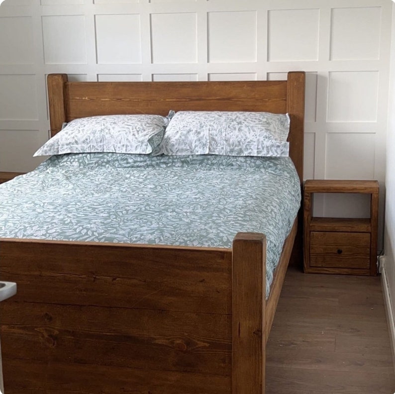 May include: A wooden bed frame with a headboard, a bedspread, and two pillows. The bedspread and pillows have a light green and white floral pattern. A matching wooden nightstand with a drawer is next to the bed.