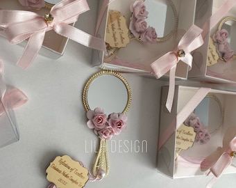 May include: A set of small, white gift boxes with pink ribbon bows. Each box contains a small, gold-framed mirror with a pink flower embellishment. The boxes are decorated with a wooden tag that reads "Reflections of Excellence Debatents Mother Daughter Tea 2022".