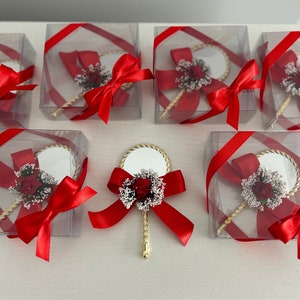 May include: A set of small, clear boxes with red ribbon bows, each containing a small, gold-handled mirror with a white and red flower embellishment.