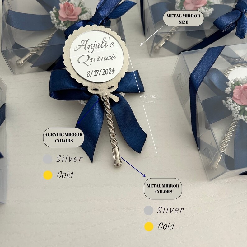 May include: A silver hand mirror with a blue ribbon and a white flower. The mirror has a personalized inscription that reads "Anjali's Quince 8/17/2024". The mirror is 4.13 inches in diameter. The mirror is available in silver or gold.