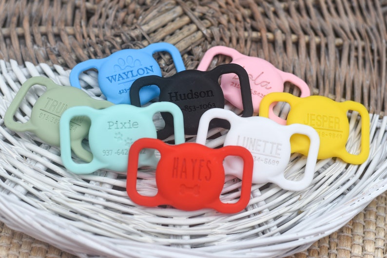 May include: A collection of colorful silicone dog collar buckles with engraved names and phone numbers. The buckles are in various colors, including red, blue, green, yellow, black, and white.