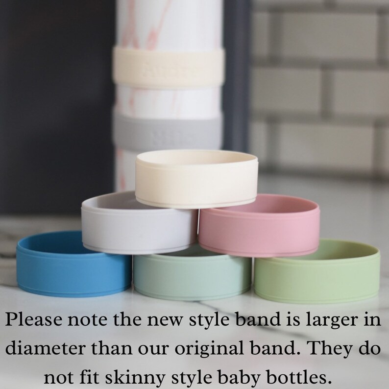 Peut inclure: Un ensemble de six anneaux en silicone de diff&eacute;rentes couleurs unies, notamment bleu, gris clair, cr&egrave;me, rose et vert clair, empil&eacute;s en pyramide. Le texte indique : Please note the new style band is larger in diameter than our original band. They do not fit skinny style baby bottles.