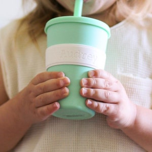Peut inclure: Un gobelet en silicone vert menthe avec un couvercle et une paille assortis, dot&eacute; d'une bande en silicone blanc autour du centre. La bande blanche est emboss&eacute;e avec le pr&eacute;nom Audrey dans une police simple et claire pour une meilleure prise.