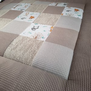 Könnte beinhalten: Eine beige und weiße Waffelstruktur-Spielmatte für Babys mit Patchwork-Design und verschiedenen Tierillustrationen. Die Matte besteht aus weichem, strukturiertem Stoff und ist perfekt für die Bauchlage oder zum Spielen.