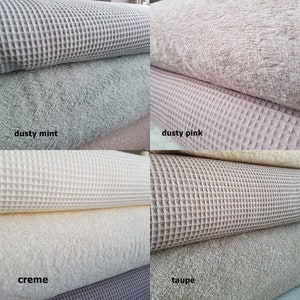 May include: Four rolls of waffle weave fabric in different colors: dusty mint, dusty pink, creme, and taupe. Each roll is folded in half and the fabric is textured.