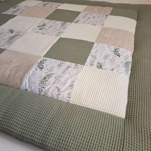 Könnte beinhalten: Eine grüne und weiße Patchwork-Spielmatte mit Blumenmuster. Die Matte besteht aus weichem, strukturiertem Stoff und ist perfekt für Babys und Kleinkinder.